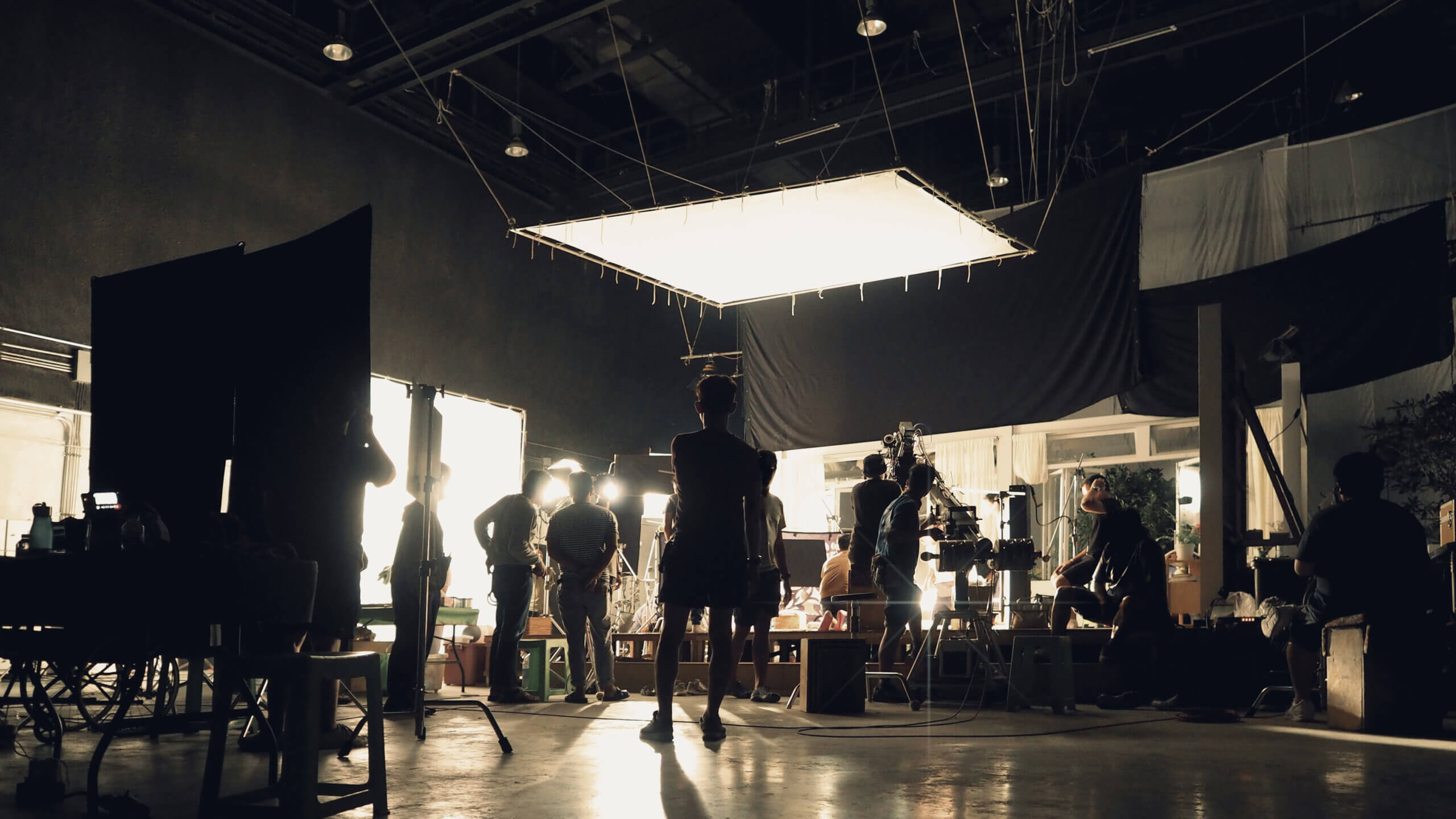 Behind the scenes of silhouette people working in big production studio with professional set and lighting for making movie film or video commercial.